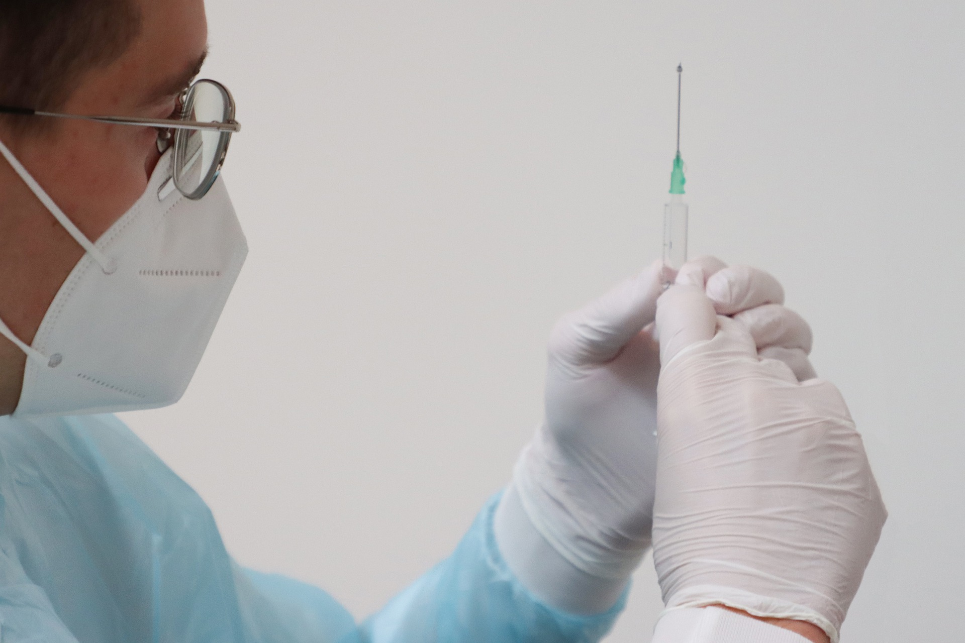 Arzt mit Maske und Handschuhen hält eine Spritze mit Impfstoff in der Hand
